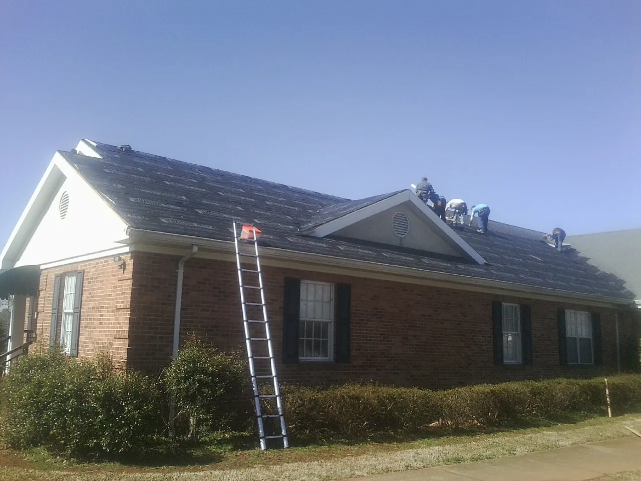 Crew tearing shingles off a brick ranch roof with a ladder set — Emergency Roof Repair work by our crew in Cayuga