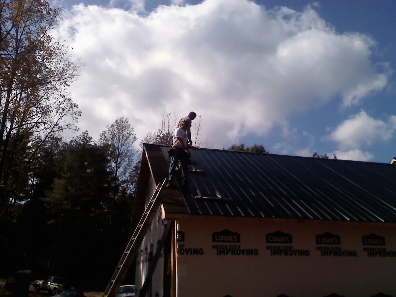 Roofer fastening dark metal panels high against a cloudy sky, from a Roof Inspection job in Cayuga