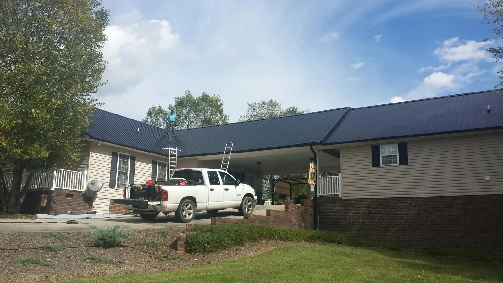 Black metal roof over a home and attached breezeway with ladders set in Cayuga