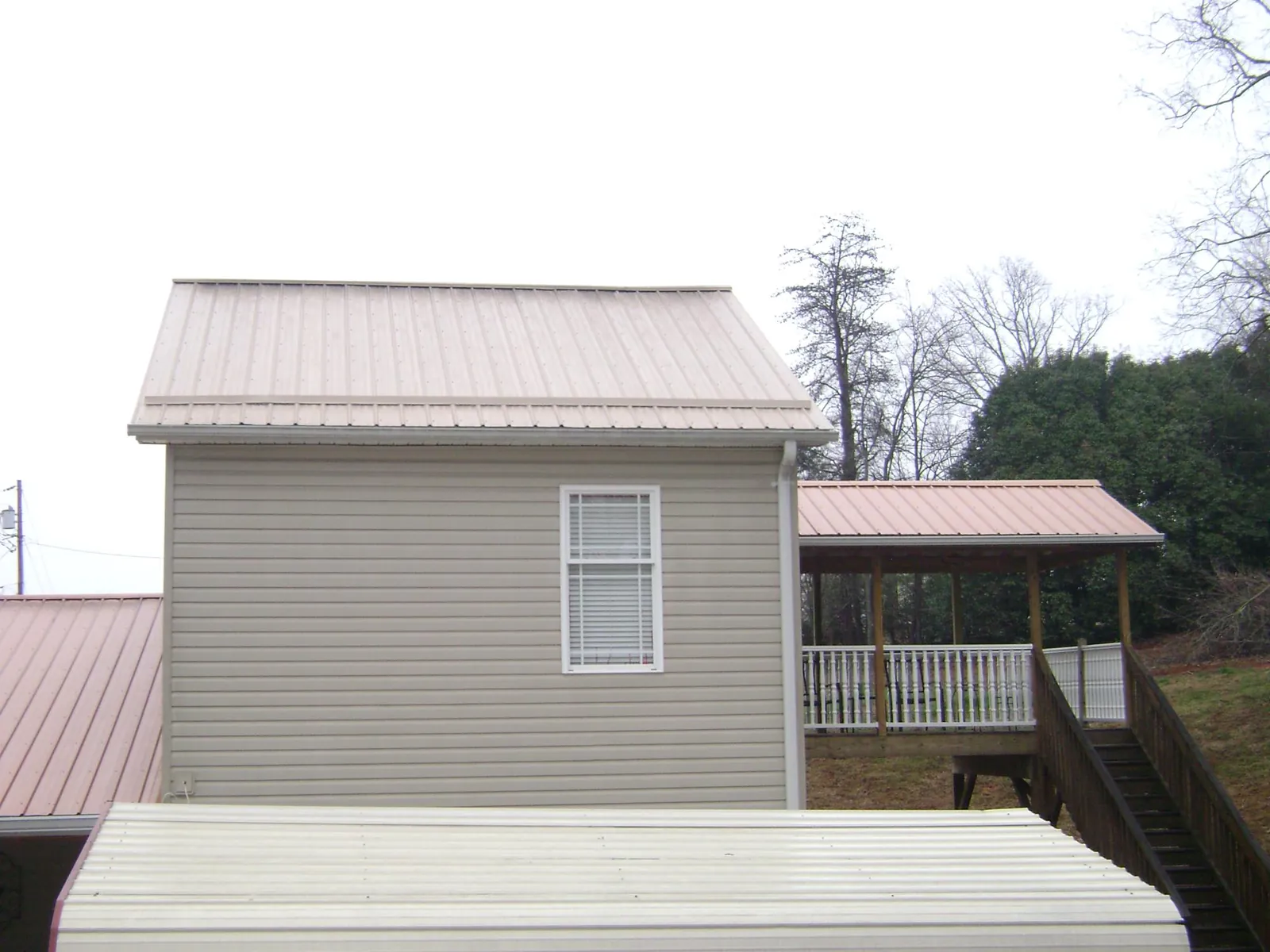 Tan metal roofs on a two story addition and attached porch, from a Roof Replacement job in Cayuga